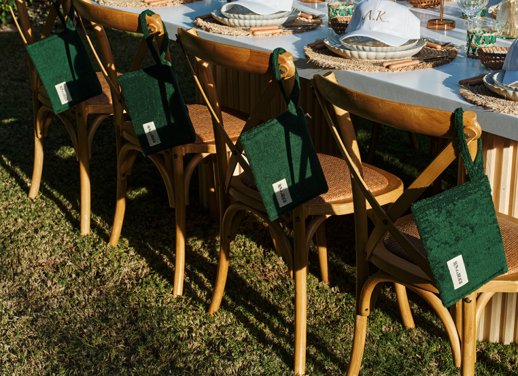 Deep green pouches hanging on wooden chairs with hats featuring the couple's initials, set up for a wedding gifts for guests.