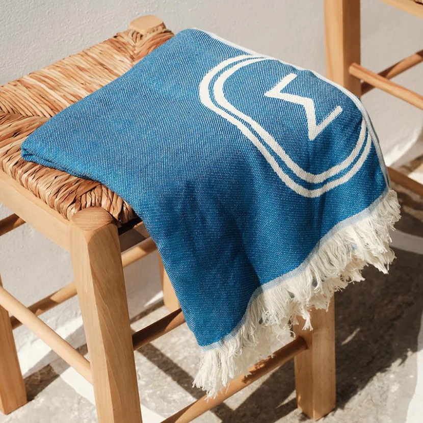 A luxury blue towel elegantly placed on a woven chair, showcasing premium quality for corporate gifts and Sergakis brand collaborations.