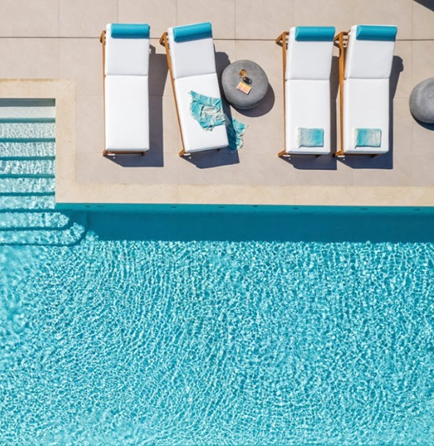Overhead view of a luxury villa poolside with white loungers, blue pool, and Sun of a Beach towels matching the pool's color.